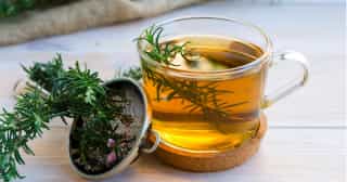 A cup of rosemary tea with fresh rosemary leaves.